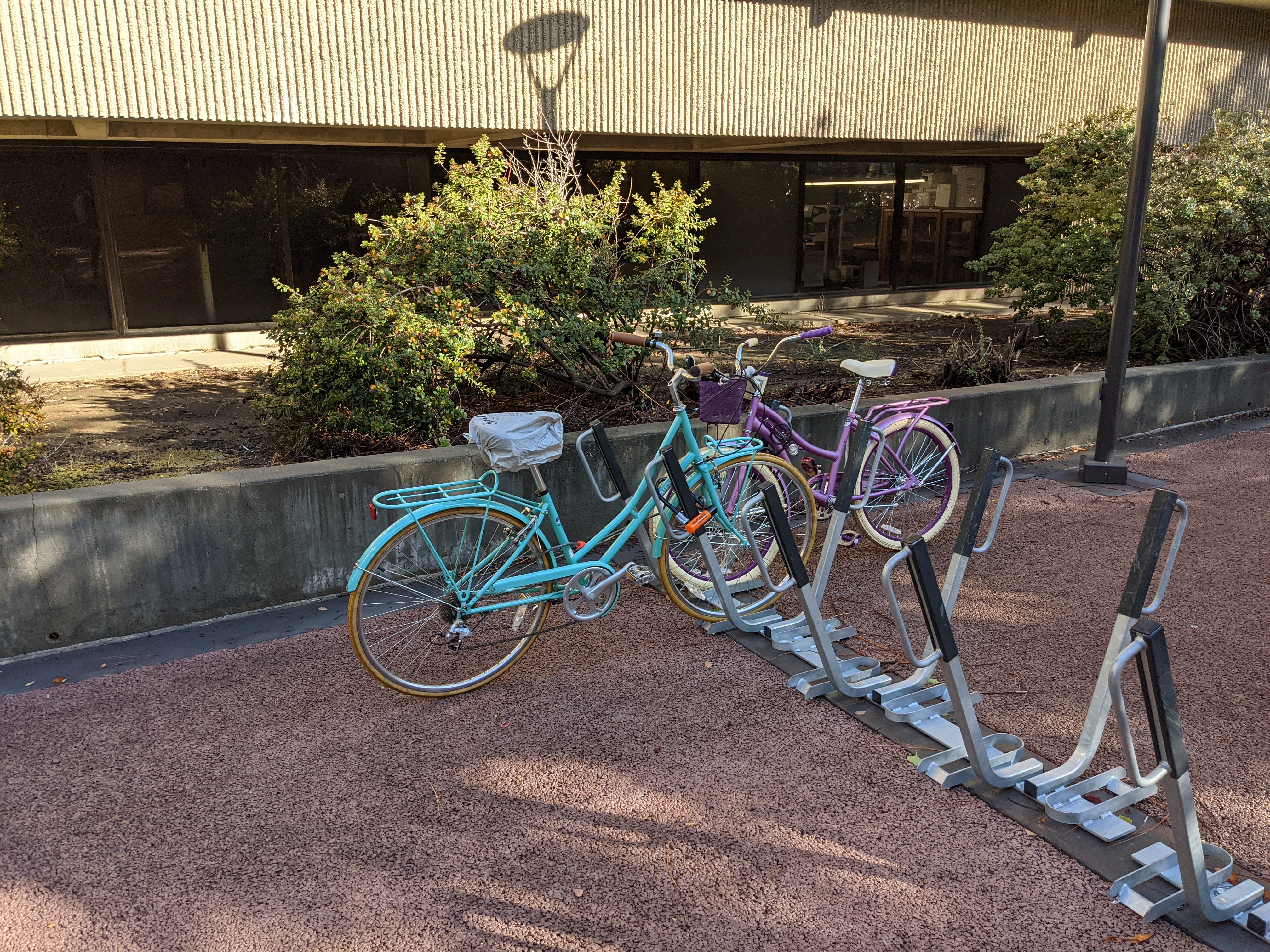 A teal bike with parked at a lightning-bolt style bike rack, with a plastic bag covering the seat.