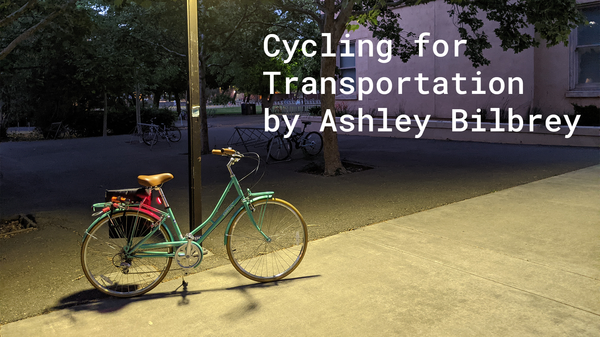 A teal city bike at night with a red tail light glowing. Text overlaid reading Cycling for Transportation by Ashley Bilbrey.